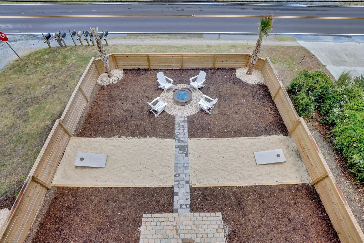 An exterior scene featuring a fire pit surrounded by Adirondack chairs, sandy yard areas, and a clear pathway, set in a relaxed and social atmosphere. The open space hints at yard activities and gatherings, which could easily include pets.