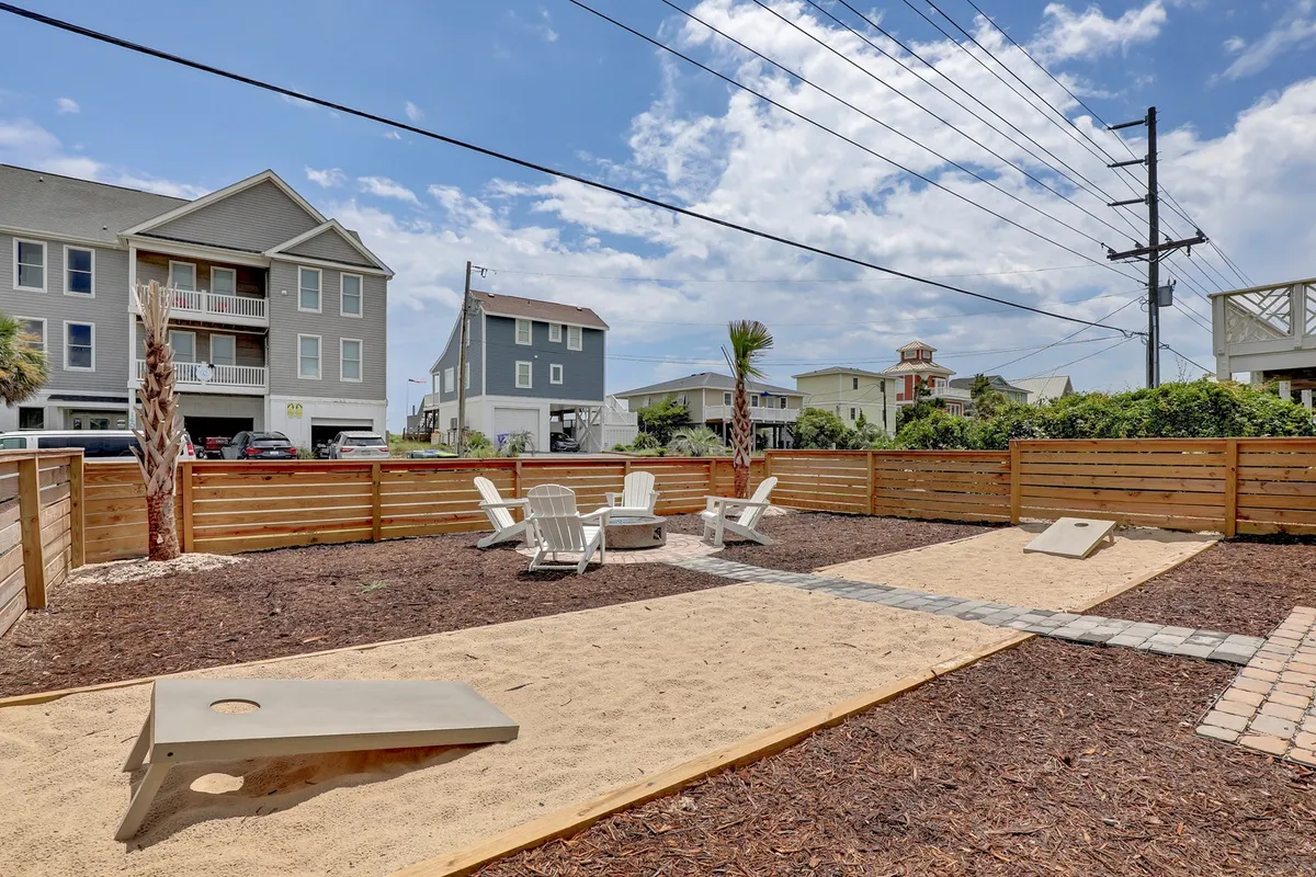 A casual outdoor space with Adirondack chairs, a sand pit, and a cornhole game set within a fenced area. The environment is playful and inviting, clearly designed for relaxation and active play, making it ideal for both children and pets. The fence offers a sense of security for families and pet owners.