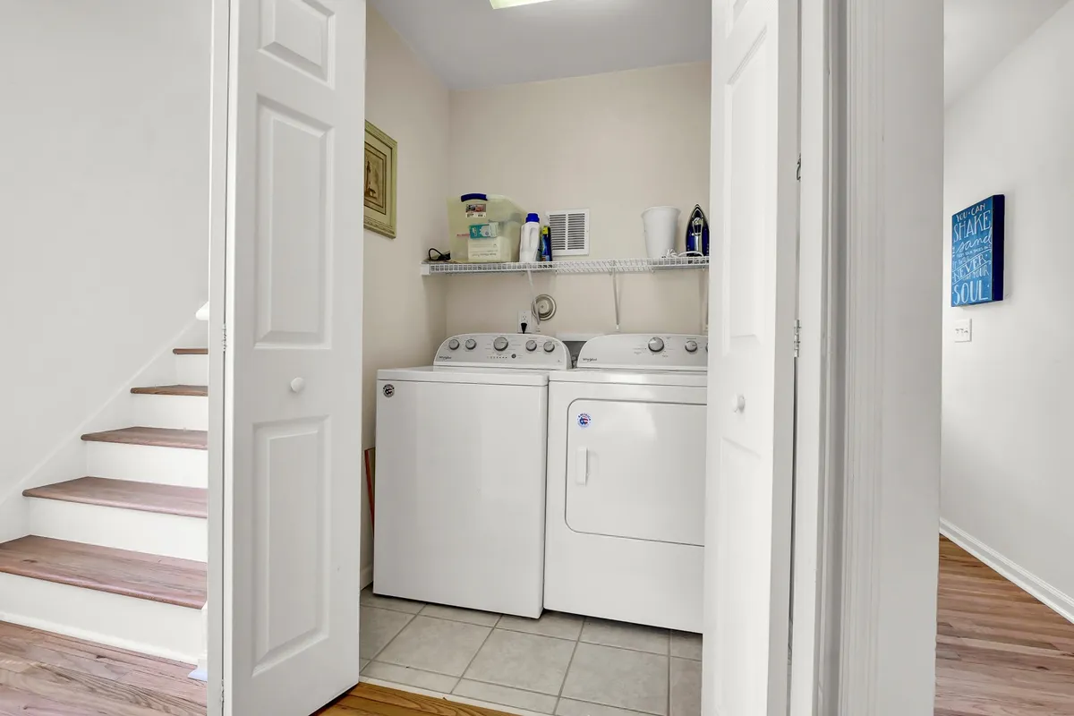 A well-organized laundry nook featuring washing machines, a shelf with laundry supplies, and a staircase nearby. The scene is practical and tidy, emphasizing convenience for guests managing their essentials.