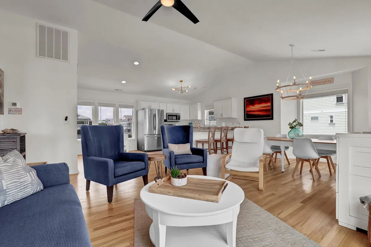 This image presents an open-concept living area seamlessly connected to a modern kitchen and dining space. Sunlight pours in through ample windows, illuminating comfortable seating and a spacious dining area designed for social gatherings and relaxation. The cohesive design and decor enhance the sense of a bright, communal hub.