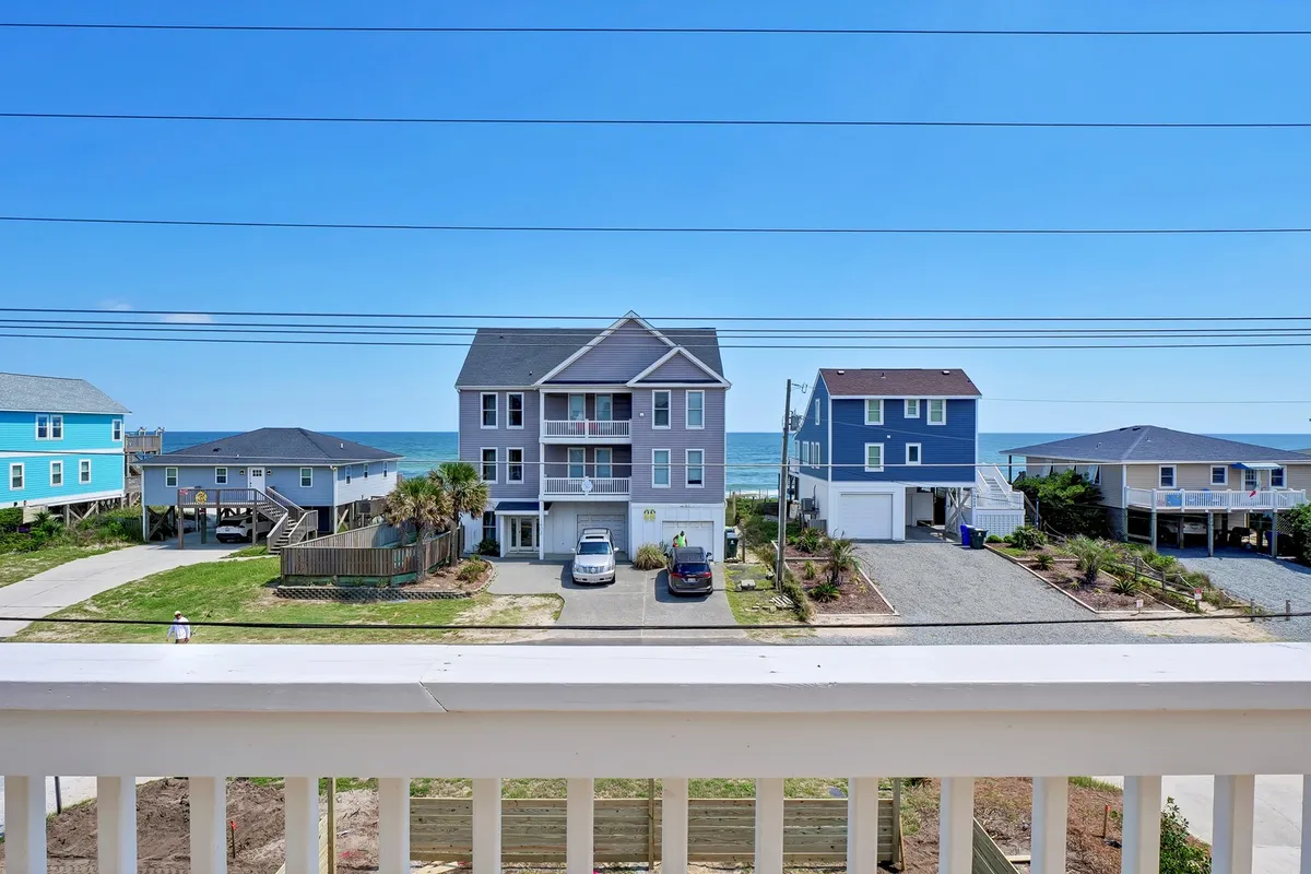 The image showcases a stunning ocean view framed by colorful beach houses, with a spacious paved driveway leading up to the property. The inviting scene hints at beach outings, family gatherings, and relaxing evenings watching sunsets.