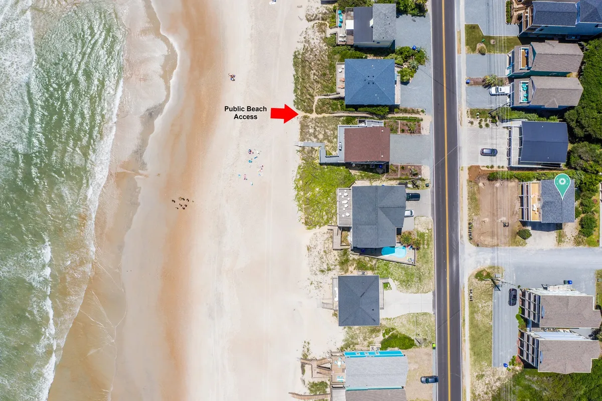 This image captures public beach access with sandy pathways, beachfront homes, and the open surf, evoking a sense of outdoor adventure and the nearby pet-friendly beach environment. The sandy stretch and relaxed scene reflect spaces where guests might walk their dogs or enjoy the coastal trails.